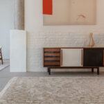 Limited-edition vloerkleed Cosmic Mongolia Papyrus met franjes in een modern interieur met houten dressoir en abstract schilderij.