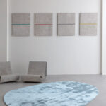 Lichtblauw Limited Edition-vloerkleed Astral Beautyberry in een minimalistisch interieur met betonnen stoelen en moderne wandkunst.