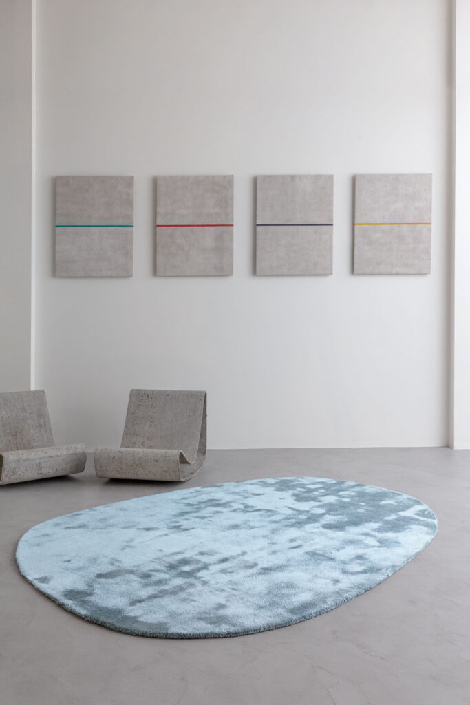 Lichtblauw Limited Edition-vloerkleed Astral Beautyberry in een minimalistisch interieur met betonnen stoelen en moderne wandkunst.