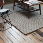 Beige limited edition vloerkleed Abaca 2 met visgraatstructuur op houten vloer, onder een houten salontafel.