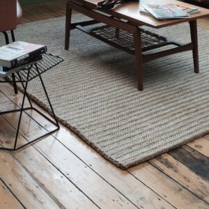 Beige limited edition vloerkleed Abaca 2 met visgraatstructuur op houten vloer, onder een houten salontafel.