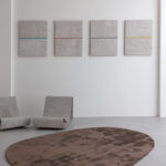 Limited edition vloerkleed Astral Cinder in een minimalistische ruimte met betonnen stoelen en abstracte wandkunst.
