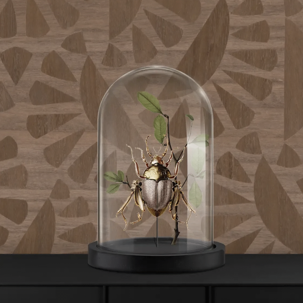 Decoratief object van een gouden kever met bladeren onder een glazen stolp, geplaatst voor een houten wand met geometrisch patroon.