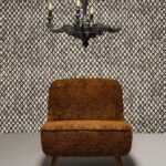 Oranje-bruin fauteuil staat voor Moooi-behang Aristo Quagga met ruitachtig zwart-wit patroon, onder een zwarte kroonluchter.
