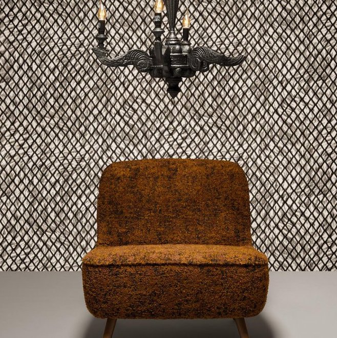 Oranje-bruin fauteuil staat voor Moooi-behang Aristo Quagga met ruitachtig zwart-wit patroon, onder een zwarte kroonluchter.