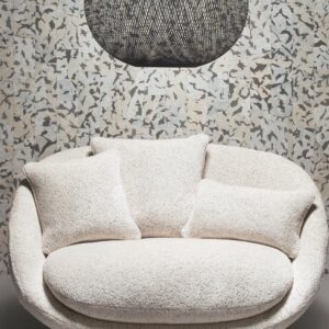 Crèmekleurige ronde loveseat met drie kussens voor een wand met Moooi-behang Armoured Boar-patroon en een zwarte hanglamp erboven.