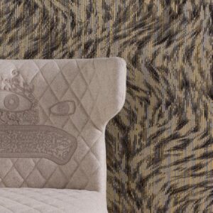 Grijze gestoffeerde stoel met geborduurd gezicht staat voor het Moooi-behang Blushing Sloth met een abstract patroon in aardetinten.