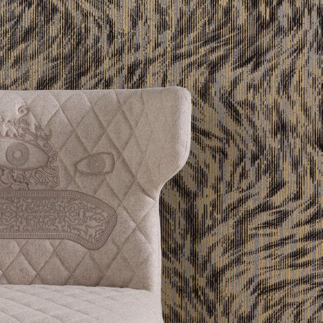 Grijze gestoffeerde stoel met geborduurd gezicht staat voor het Moooi-behang Blushing Sloth met een abstract patroon in aardetinten.