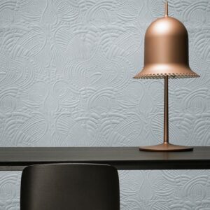 Mat lichtblauw Moooi Dodo Pavone-behang met reliëfpatroon achter een zwarte tafel en een koperen designlamp.