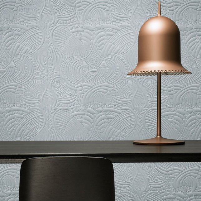 Mat lichtblauw Moooi Dodo Pavone-behang met reliëfpatroon achter een zwarte tafel en een koperen designlamp.