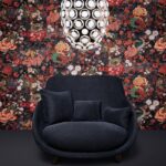 Donkerblauwe fauteuil met kussens voor een kleurrijk, bloemrijk Moooi behang uit de Tokyo Blue Rendezvous collectie en een moderne, ronde hanglamp erboven.