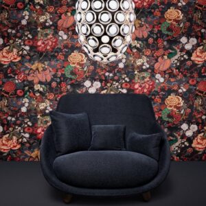Donkerblauwe fauteuil met kussens voor een kleurrijk, bloemrijk Moooi behang uit de Tokyo Blue Rendezvous collectie en een moderne, ronde hanglamp erboven.