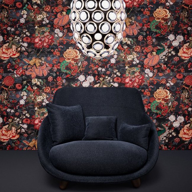 Donkerblauwe fauteuil met kussens voor een kleurrijk, bloemrijk Moooi behang uit de Tokyo Blue Rendezvous collectie en een moderne, ronde hanglamp erboven.