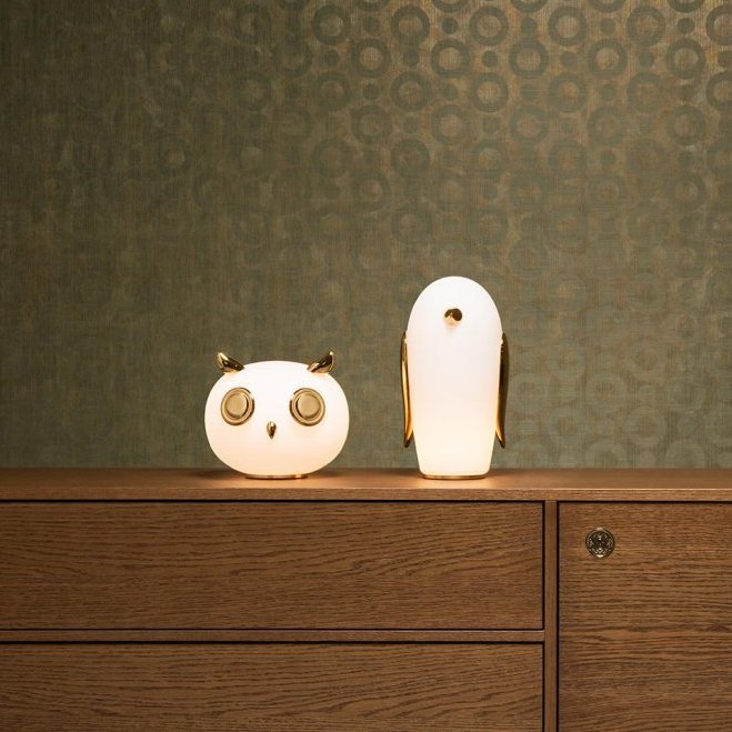 Twee decoratieve lampen in de vorm van een uil en een vogel staan op een houten kast voor behang in het Moooi Umbrella Squid-patroon.
