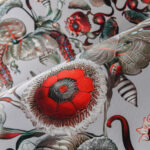 Gedetailleerde close-up van het Moooi Coccinella Bella MO5010 behang met een fantasierijk bloem- en insectenpatroon in rood, groen en grijstinten.