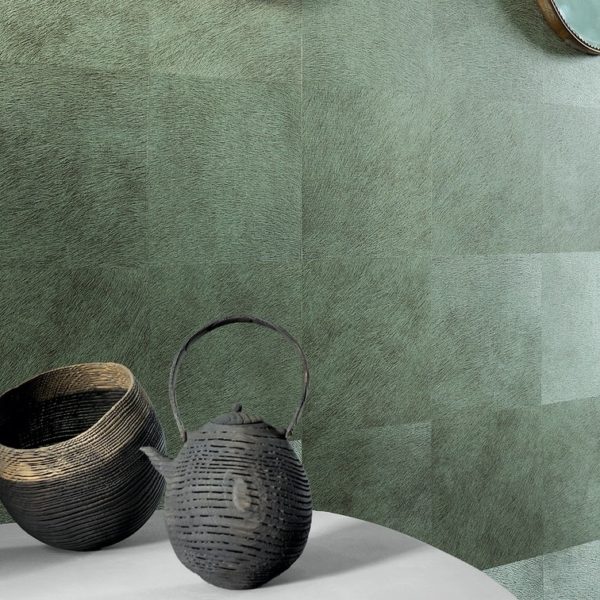 Groene wandbekleding Movida VP 625 met een textuurpatroon, gecombineerd met rustieke zwarte mand en theepot op een ronde tafel.