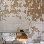 Glazen bureau met witte draadstoel tegen een artistieke muur met verweerd patroon en roze lijn, bij de opening van Lombok.