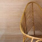 Rotan Sinabaye-stoel met een hoge, gebogen rugleuning tegen een beige muur.