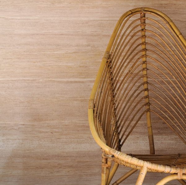 Rotan Sinabaye-stoel met een hoge, gebogen rugleuning tegen een beige muur.