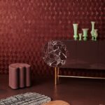 Moderne interieursetting met een donkerrode 3D-patroonmuur, een glanzend dressoir met marmeren detail en groene vazen.