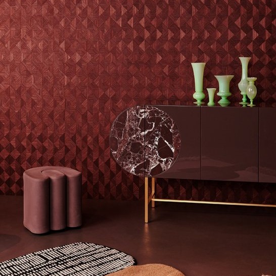Moderne interieursetting met een donkerrode 3D-patroonmuur, een glanzend dressoir met marmeren detail en groene vazen.