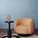 Beige designfauteuil naast een zwarte bijzettafel met vaas, voor een blauw geometrisch Optique2-M40D-2 behang.