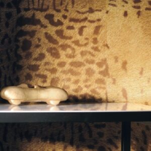 Gouden miniatuurauto op een plank voor een wand met panterprint.