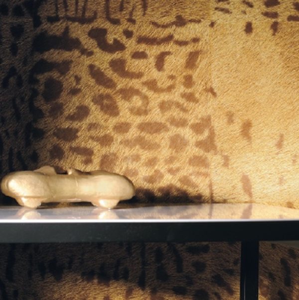 Gouden miniatuurauto op een plank voor een wand met panterprint.