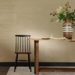 Houten tafel met vaas en takken naast een zwarte houten stoel tegen een beige Perles Jade muur.