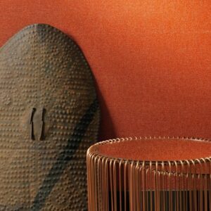 Decoratief interieur met een rood-oranje textuurmuur, metalen draadtafel en een donker decoratief schild met reliëfpatroon.