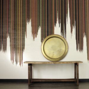 Houten tafel met ronde gouden schaal tegen een muur met kleurrijk verticaal strependessin, getiteld Perles Parade de Samba.