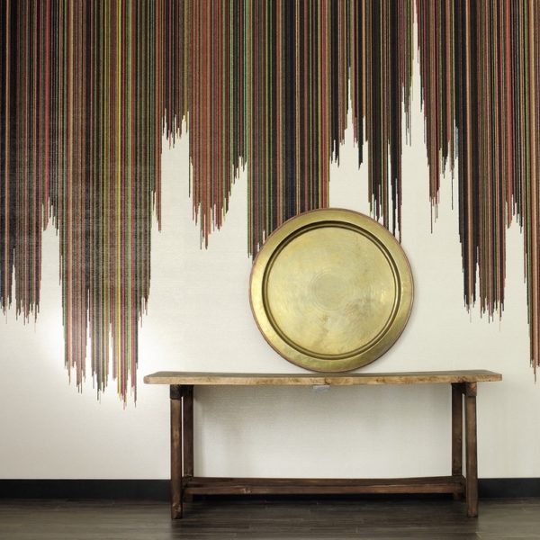Houten tafel met ronde gouden schaal tegen een muur met kleurrijk verticaal strependessin, getiteld Perles Parade de Samba.