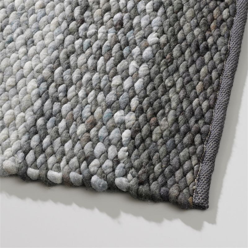 Hoek van het Perletta Limone Fade Green wollen vloerkleed met grove, handgeweven structuur in groen- en grijstinten.