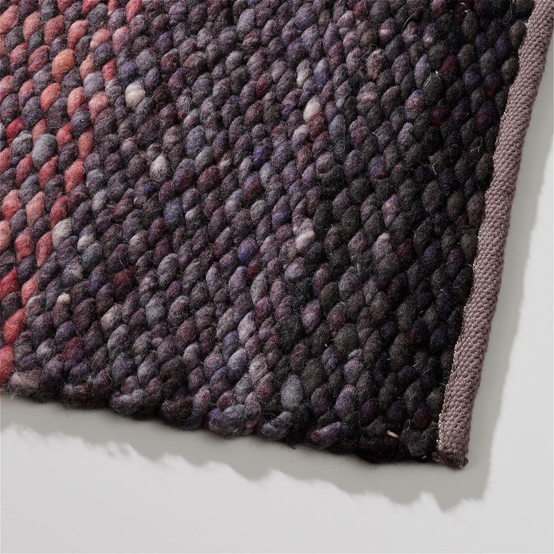 Close-up van een Perletta Limone Fade Purple wollen vloerkleed met een grof geweven structuur in paarse en roodtinten.