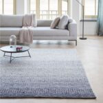 Sfeervolle woonkamer met een Perletta Limone Fade vloerkleed in grijsblauwe tinten voor een lichte bank en salontafel.