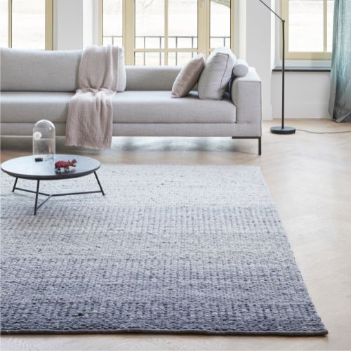 Sfeervolle woonkamer met een Perletta Limone Fade vloerkleed in grijsblauwe tinten voor een lichte bank en salontafel.
