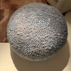 Ronde, blauw gemêleerde Perletta pouffe van gevlochten wol op een lichte vloer.