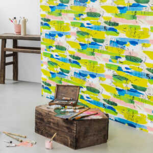 Kunstzinnige kamer met het kleurrijke behang "Les Amoureux" van Pierre Frey, omlijst door schildermaterialen en rustiek houten meubilair.