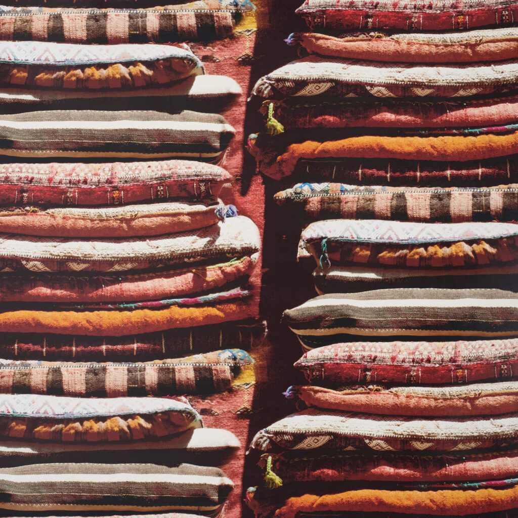 Gestapelde, kleurrijke kussens met etnische patronen in een bazaarstijl, gebaseerd op het Pierre Frey Le Grand Bazar ontwerp.