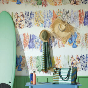 Zomerse interieursetting met Pierre Frey La Baignade-behang vol kleurrijke badkleding, een groene surfplank, strandaccessoires en een blauw tafeltje.