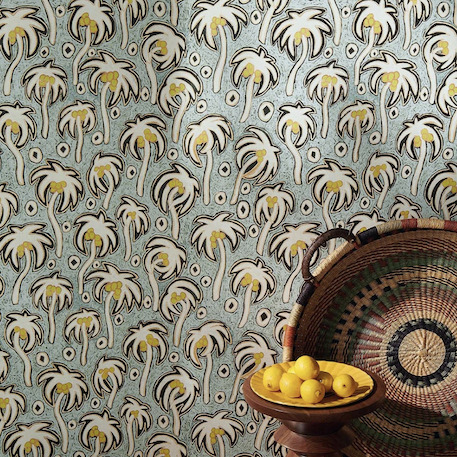Decoratief Pierre Frey Varaderos behang met gestileerde palmboomprint in geel en wit, met een mand vol citroenen op de voorgrond.