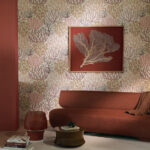 Sfeervolle woonkamer met Pierre Frey behang Acropora FP009001 in koraalmotief, warme rood- en aardetinten en een modern kunstwerk aan de muur.