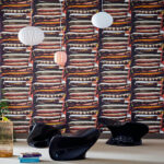 Moderne interieursetting met Pierre Frey-behang FP624001 Le Grand Bazar, waarop kleurrijke stapels kussens zijn afgebeeld.