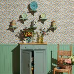 Groen dressoir en houten stoel tegen Pierre Frey-behang Les Anémones met kleurrijk keramiek en bloemen.
