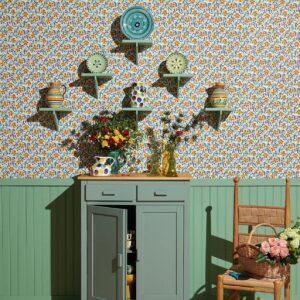 Groen dressoir en houten stoel tegen Pierre Frey-behang Les Anémones met kleurrijk keramiek en bloemen.