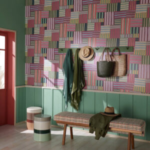 Woonkamer met kleurrijk Pierre Frey Transat FP 013002 behang, groene lambrisering, een bankje en wandhaken met accessoires.