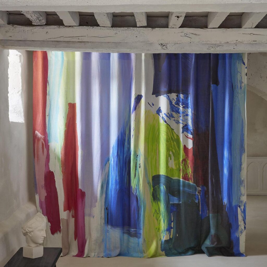 Gordijn van Pierre Frey-stof Karma F3729001 met felgekleurde, abstracte penseelstreken in een lichte, rustieke ruimte.
