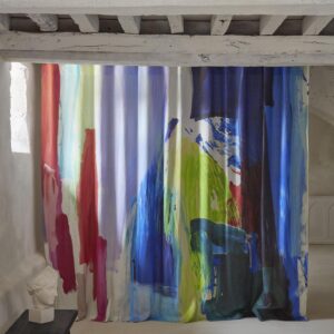 Gordijn van Pierre Frey-stof Karma F3729001 met felgekleurde, abstracte penseelstreken in een lichte, rustieke ruimte.