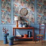 Sfeervolle woonkamer met Pierre Frey behang "Pleine Mer" in blauw en roodtinten, gecombineerd met kleurrijke meubels en maritieme decoratie.