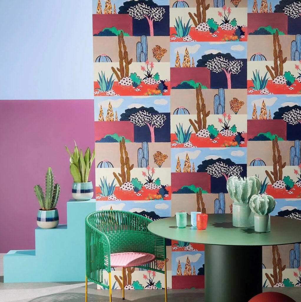 Kleurrijke interieursetting met Pierre Frey Riad-behang met woestijnmotieven, omringd door planten en felgekleurde meubels.